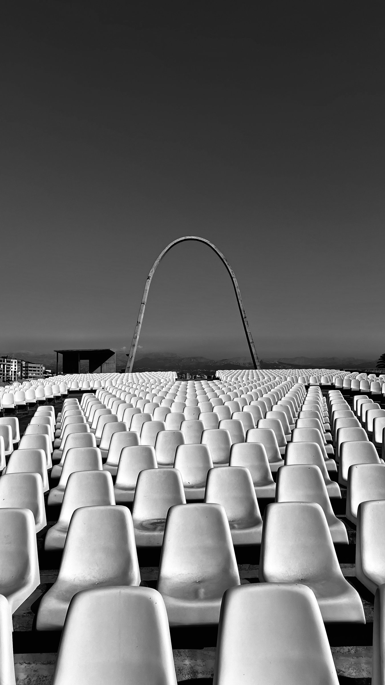 Empty stadium seating with a soaring arch in the distance — black and white
