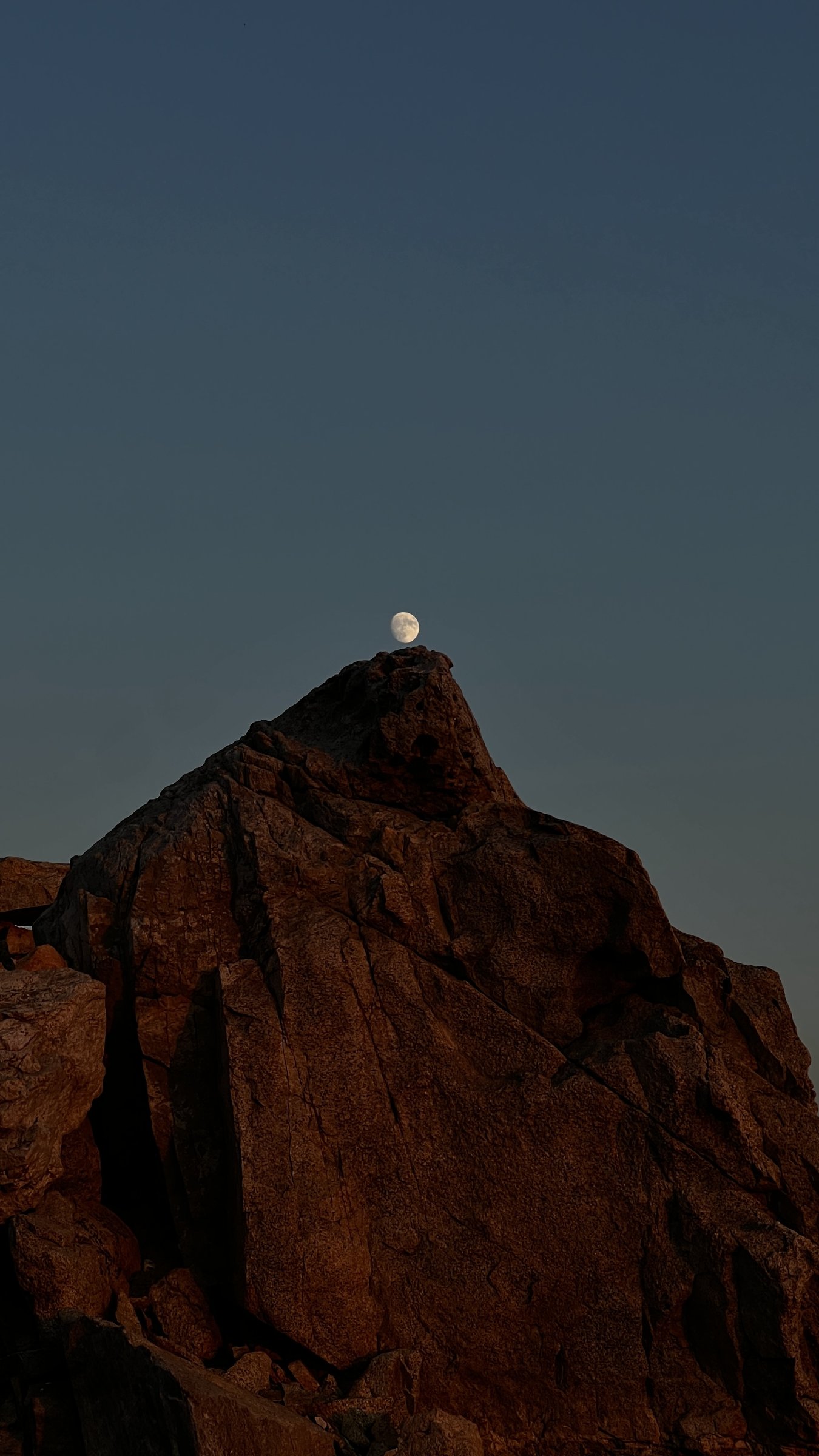 Moon rising behind a rough rock outcrop at dusk