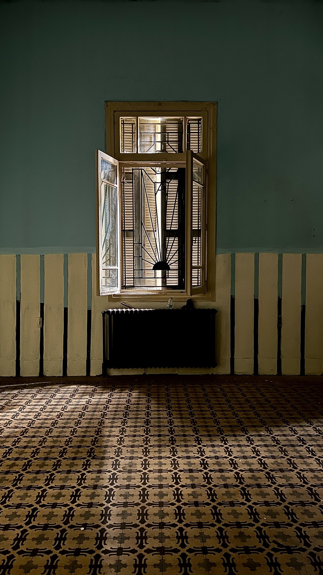 Open shuttered window over patterned cement tiles in a worn Beirut room