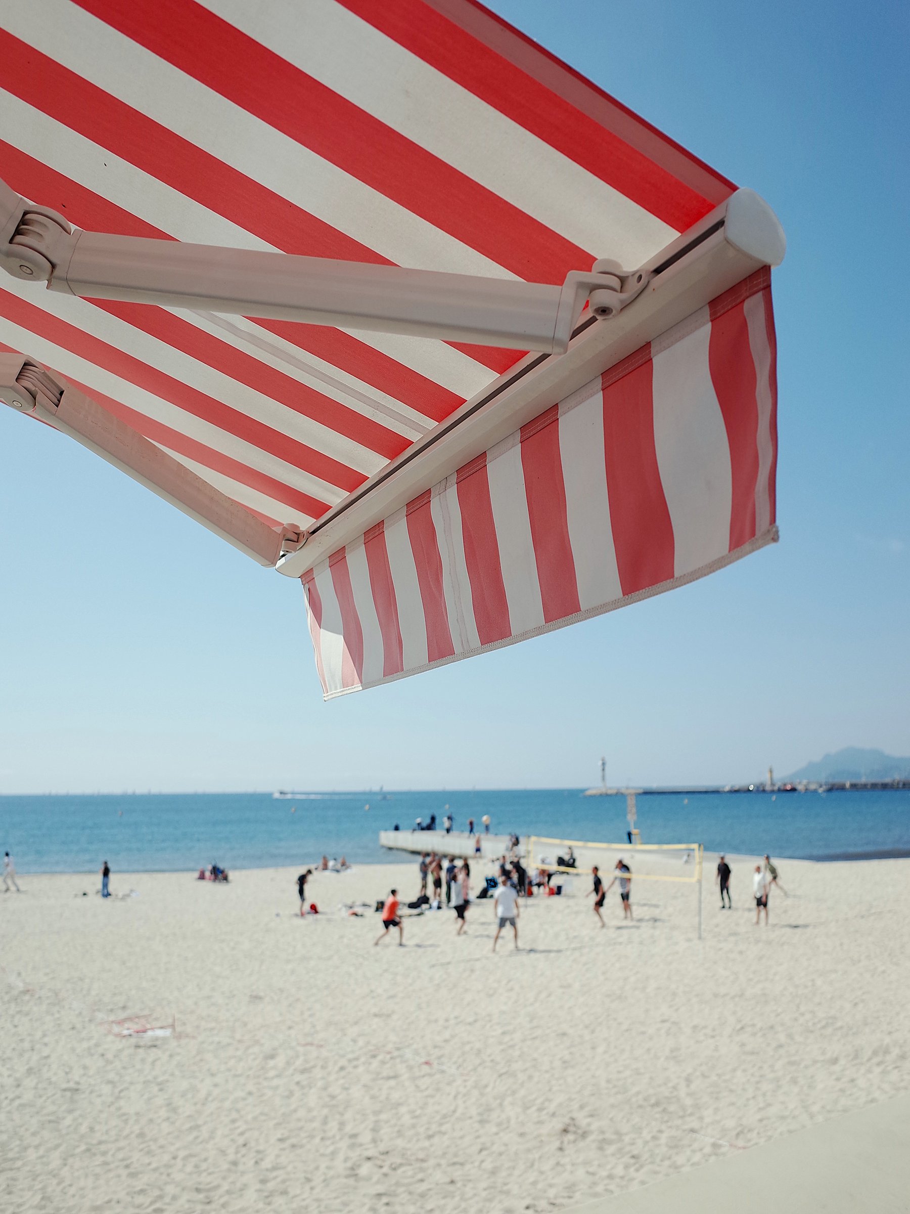 Red and white beach awning, volleyball game in the background